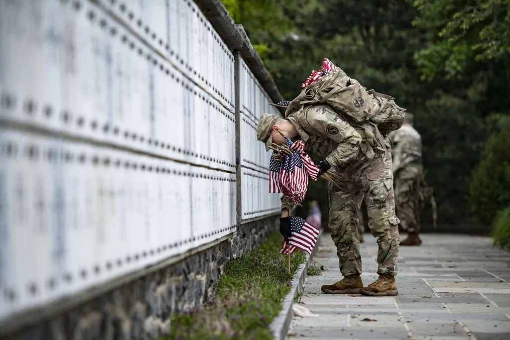 Service members kneel to place small U.S. flags at gravesites during Flags-In at Arlington National Cemetery